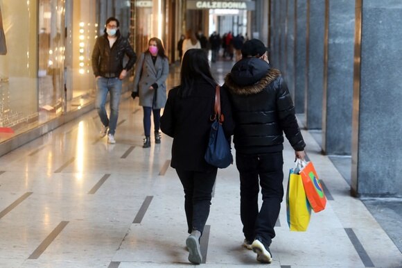 Due persone, di spalle, camminano in una via dello shopping con sacchetti colorati in mano