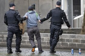 Un uomo visto di spalla preso in consegna da due poliziotti