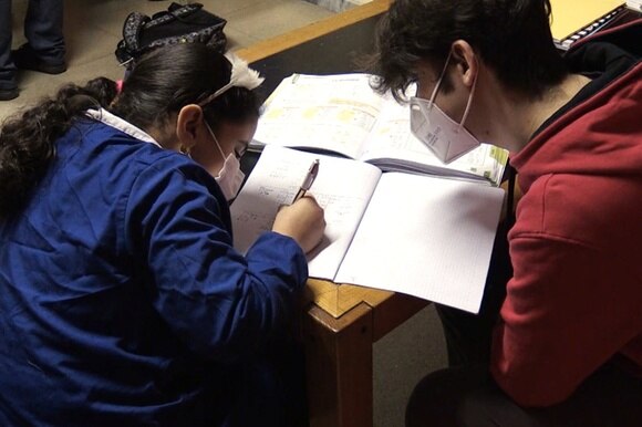Una bambina seguita da un insegnante, mentre fa i compiti.
