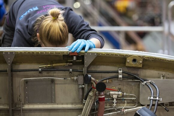 Giovane donna con tuta blu e guanti lavora a un dispositivo meccanico in uno stabilimento
