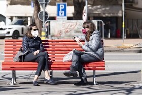 Due donne con la mascherina sedute su una panchina.