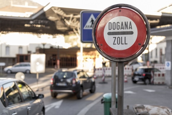 Primo piano di cartello stradale Dogana-Zoll ; si vede, sfocata, la dogana di Chiasso strada
