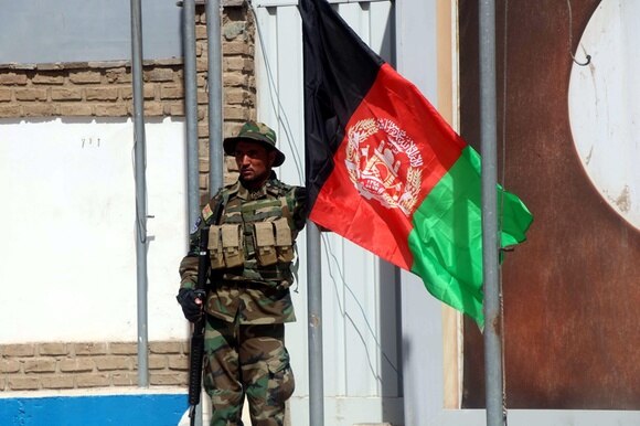 Un soldato dell esercito regolare afghano davanti a una bandiera del suo paese.