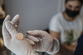 primo piano di mani con guanti che prelevano con una siringa da una fiala una dose di vaccino