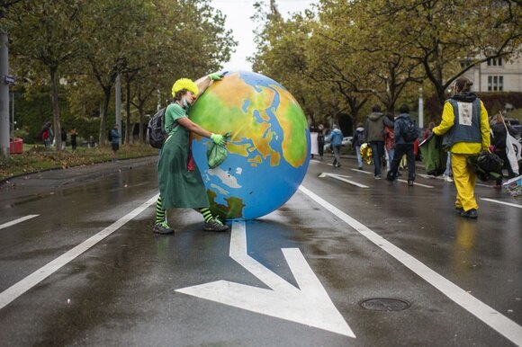 Un attivista vestito da pagliacco che abbraccia un globo gigante.