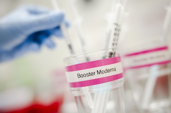 Un bicchiere con la scritta Booster Moderna, con diverse siringhe con il vaccino pronte per essere utilizzate.