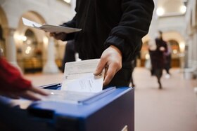 inquadratura di mano di uomo che inserisce amteriale di voto in urna