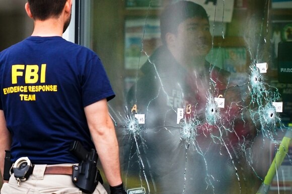 poliziotto davanti a una vetrina crivellata di colpi