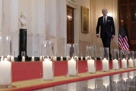 Joe Biden cammina in un corridoio della Casa Bianca con candele a lato.