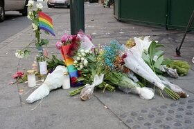 mazzi di fiori e bandierine arcobaleno appoggiati sul cemento