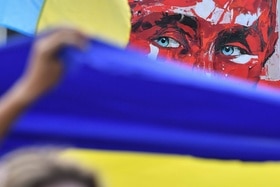 Bandiera ucraina in primmo piano e sullo sfondo il ritatratto di Putin.