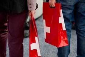 due persone tengono in mano sacchetti di carta con la bandiera svizzera