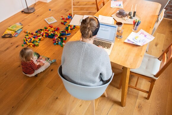 donna seduta a un tavolo con computer e bambina seduta per terra
