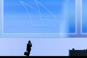 uomo con valigetta in mano partla al telefono, in piedi controluce sullo sfondo del logo di credit suisse
