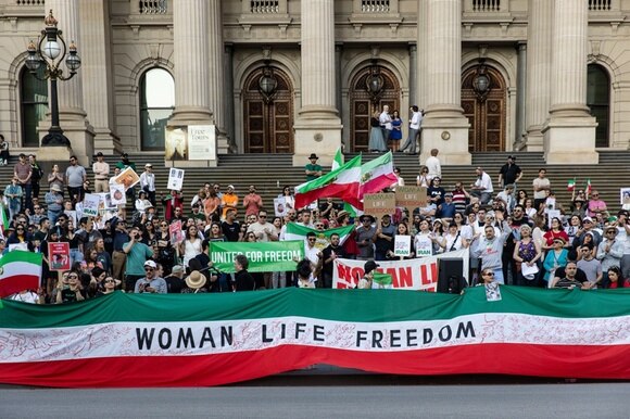 manifestanti in australia tengono striscione con scritta woman life freedom su bandiera iraniana